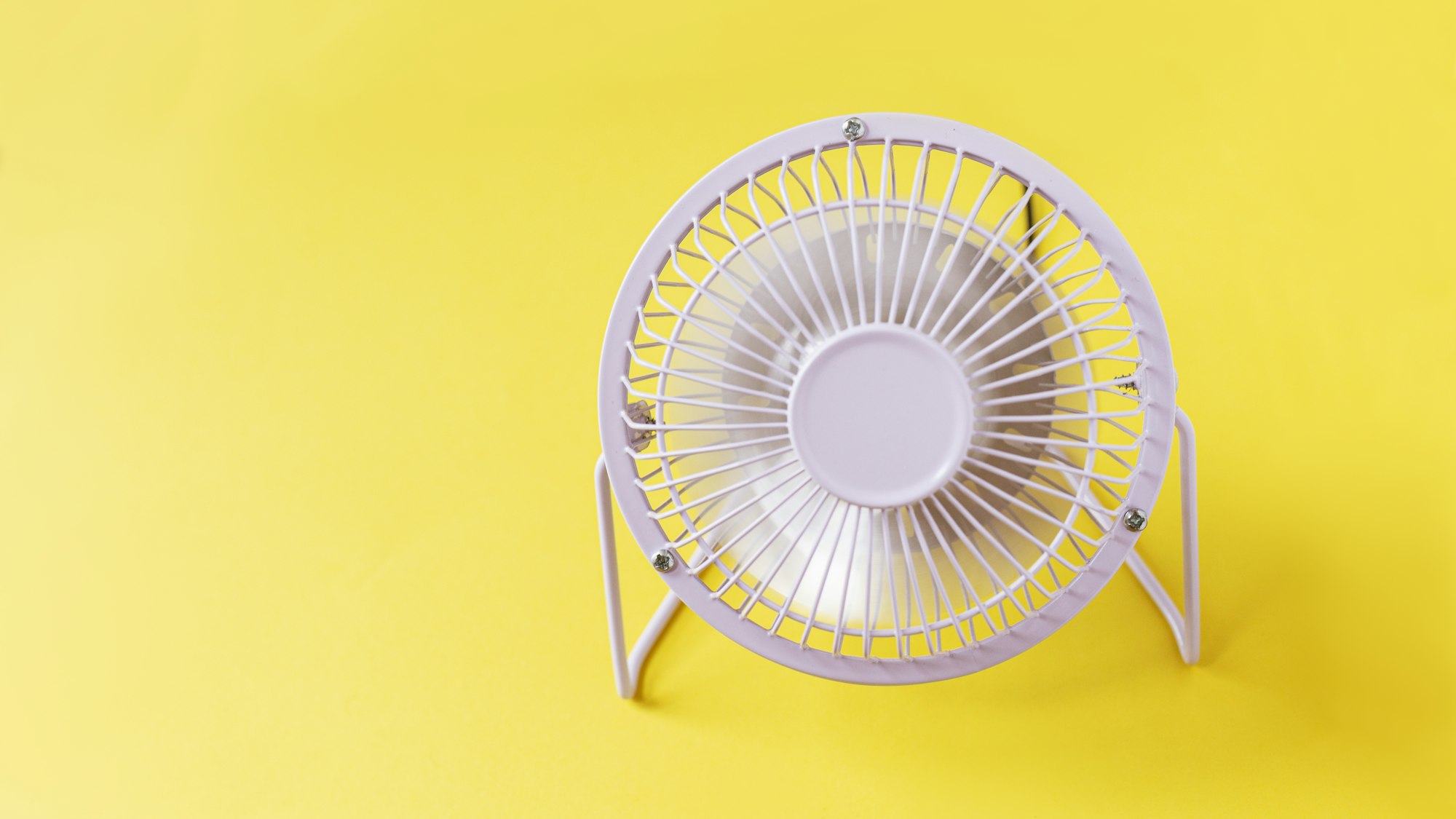 metal fan stands on a yellow background and blows. Heat and airflow, creative